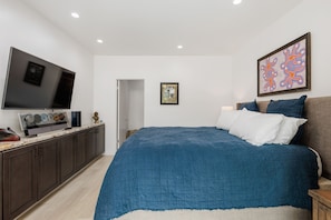 A bedroom with a large bed, a flat-screen TV, a framed picture, and a door.