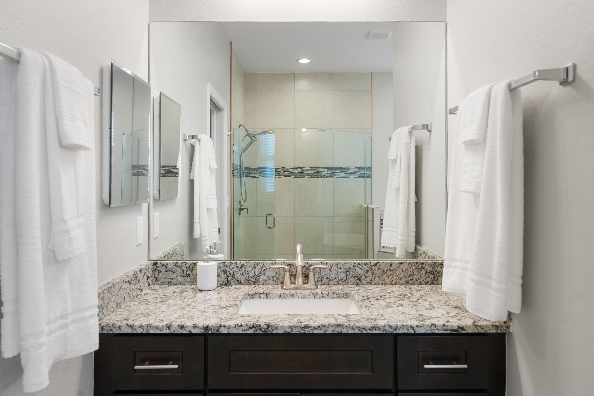 A modern bathroom with a granite countertop, a sink, a mirror, and a glass-enclosed shower.