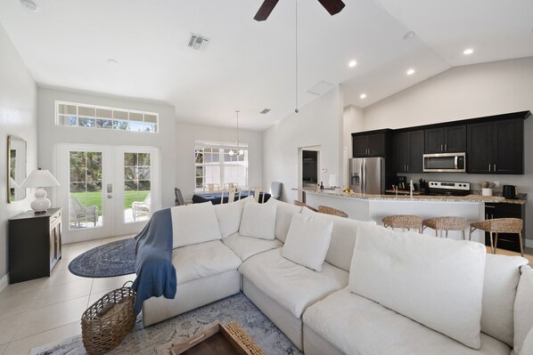 A spacious living area with a large white sectional sofa, a kitchen with dark cabinets, and a dining area with wicker chairs. - PRIVATE, SPACIOUS, COZY & CLEAN!! CLOSE TO EVERYTHING. GULF COAST 20 MIN AWAY 🏝 (North Port)