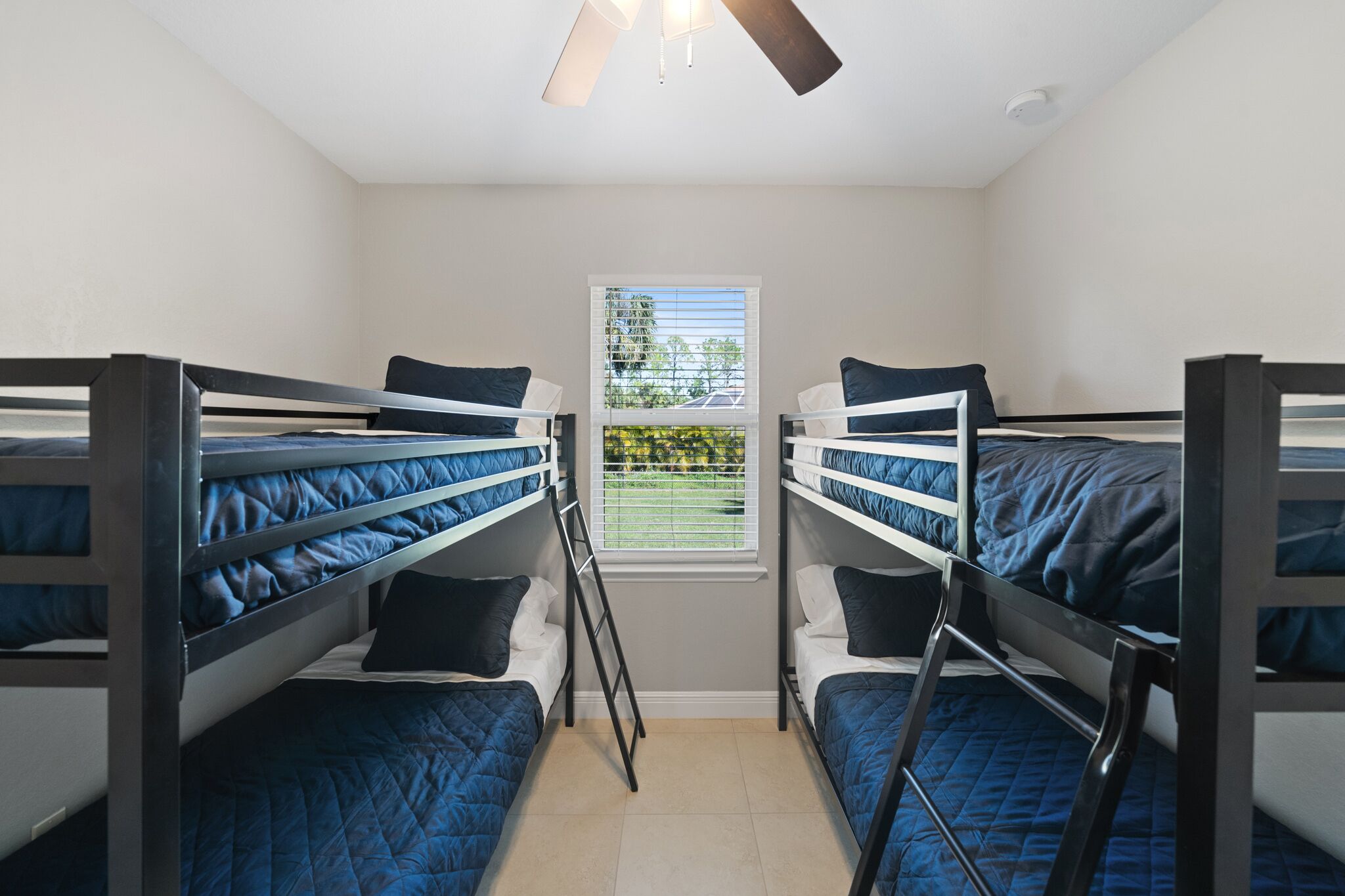 A dormitory room with bunk beds, a window with blinds, and a ceiling fan.