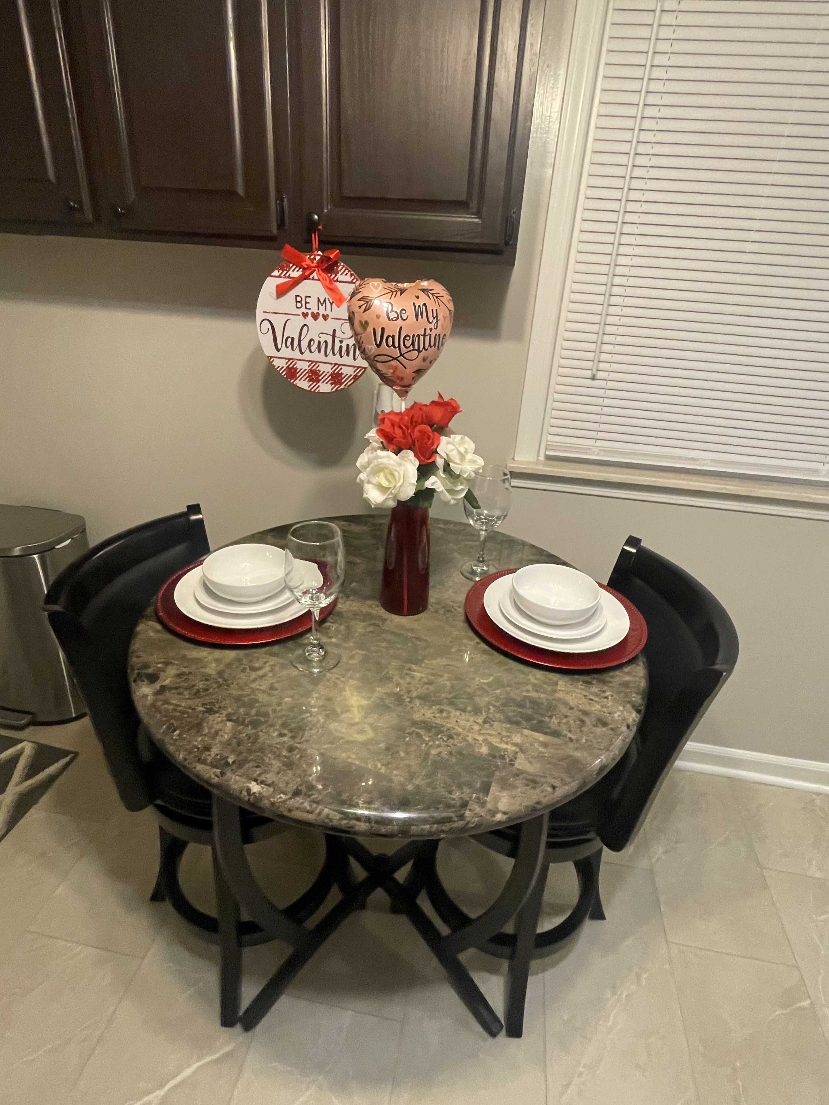 Una mesa de comedor dispuesta con platos blancos, servilletas rojas y un florero con flores rojas y blancas.