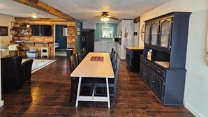 A spacious living area with a dining table, a kitchen with dark cabinetry, and a ceiling fan.