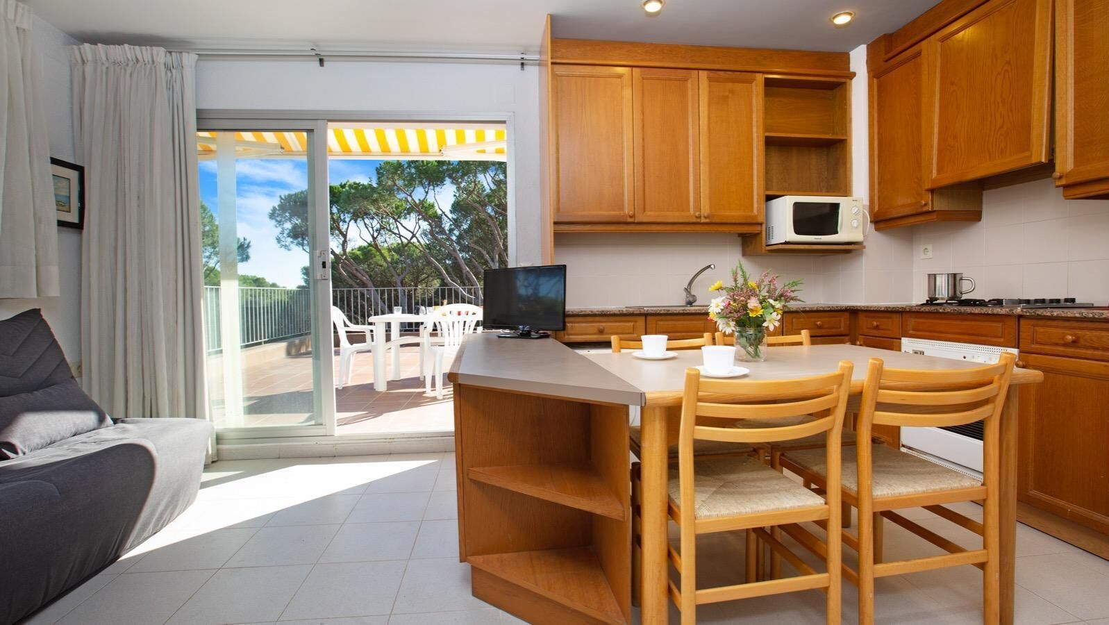Una cocina moderna con armarios de madera, un comedor con mesa y sillas, un televisor de pantalla plana y vistas al exterior.