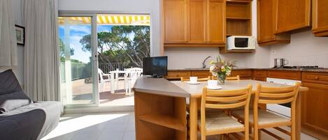 A modern kitchen with wooden cabinets, a dining area with a table and chairs, a flat-screen TV, and a view of the outdoors.
