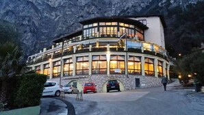 Un hotel de varios pisos con fachada curva, amplias ventanas y montañas al fondo.