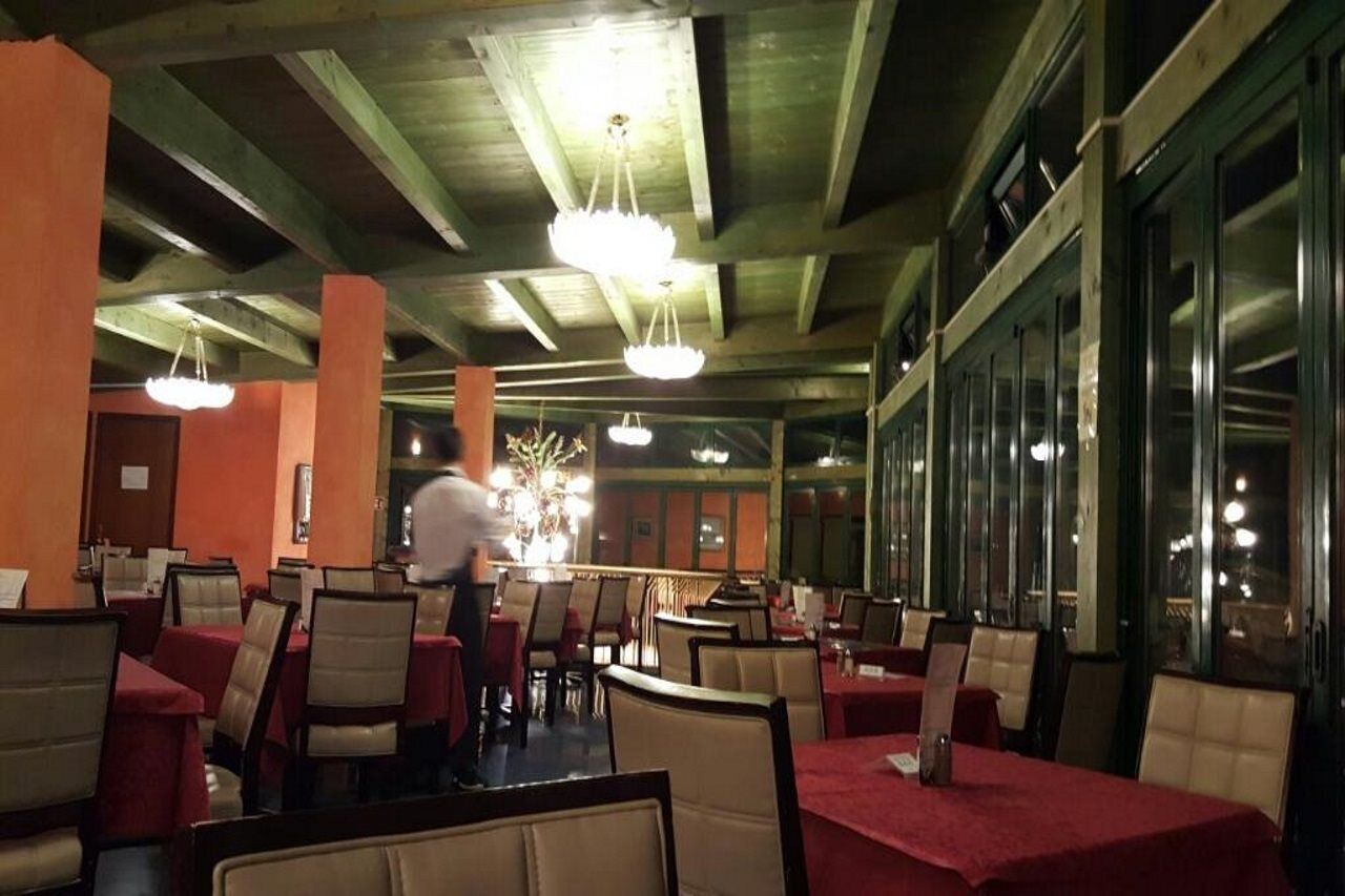 A restaurant with booths and tables, a waiter, and a chandelier.