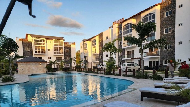 A swimming pool surrounded by lounge chairs and a building with multiple balconies.