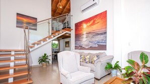 A spacious living area with a staircase, a large painting of a sunset, and a comfortable seating arrangement.