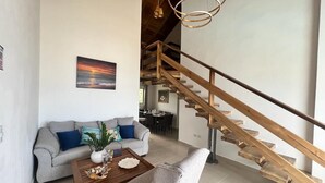 A spacious living area with a wooden staircase, a grey sofa, a coffee table, and a painting of a sunset.