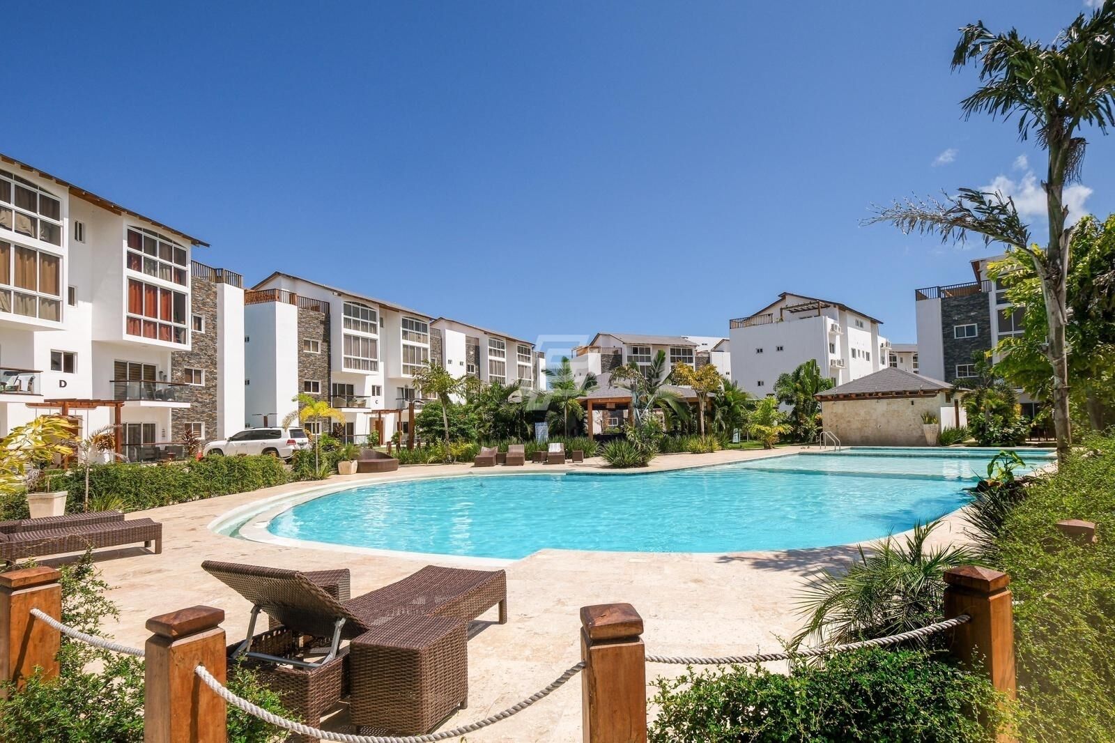 A pool area with lounge chairs and a clear blue pool surrounded by modern buildings.