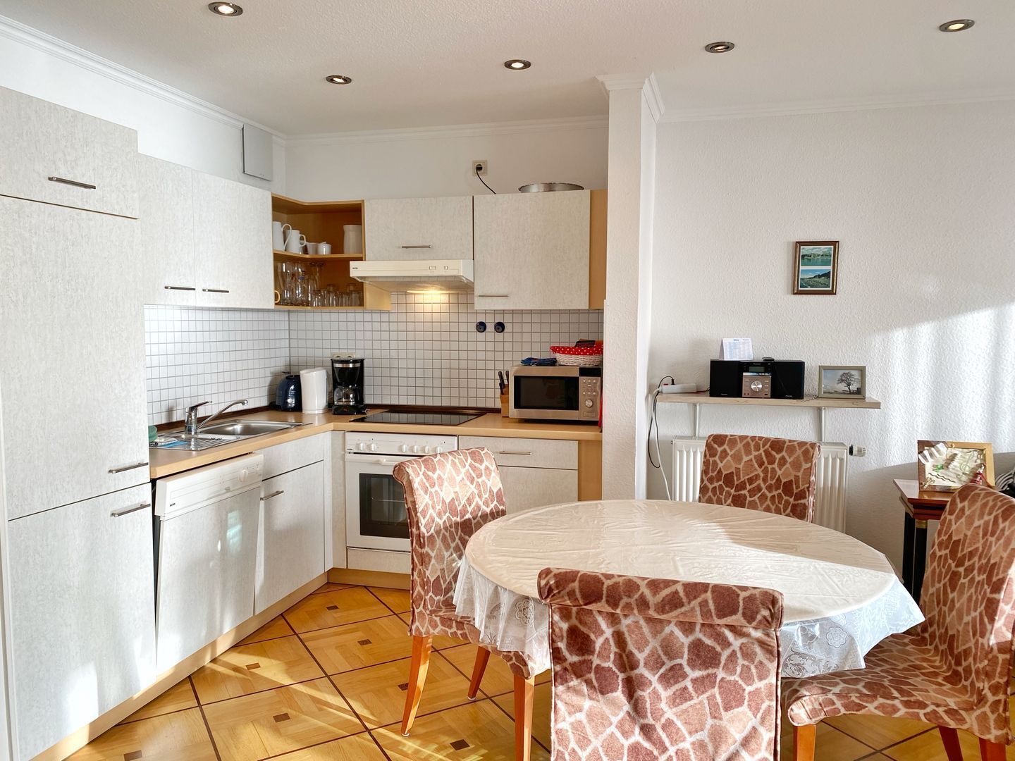 A compact kitchen with white cabinets, a microwave, and a coffee maker. There is a round table with giraffe-patterned chairs.