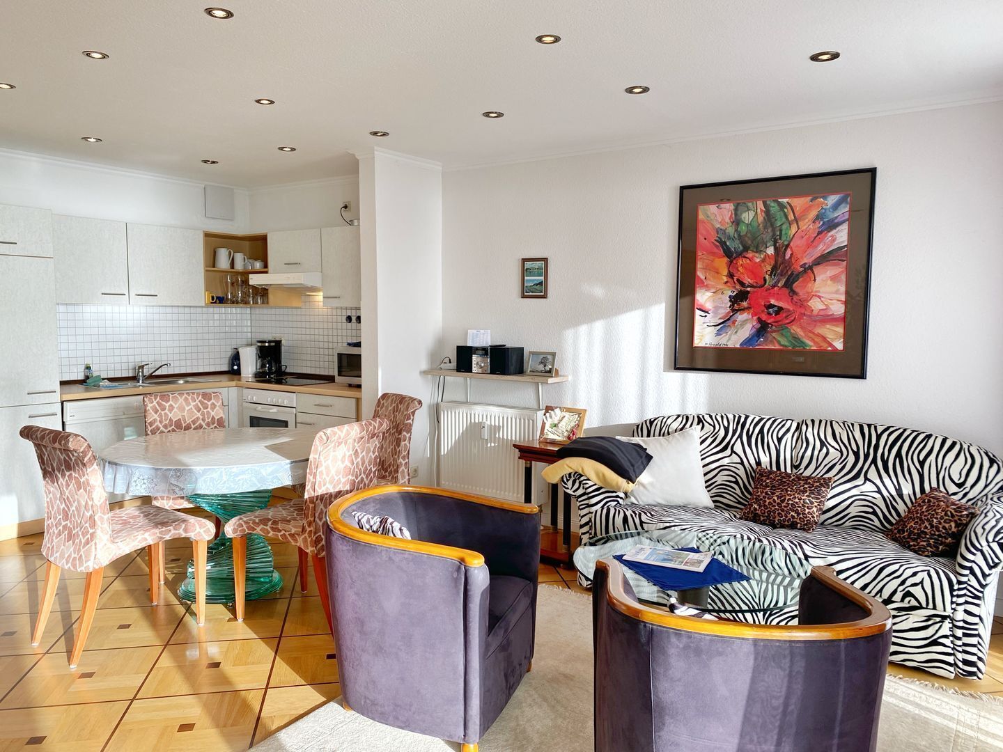 Un salon moderne avec un canapé à motifs zébrés, une table à manger avec des chaises, et une cuisine en arrière-plan.