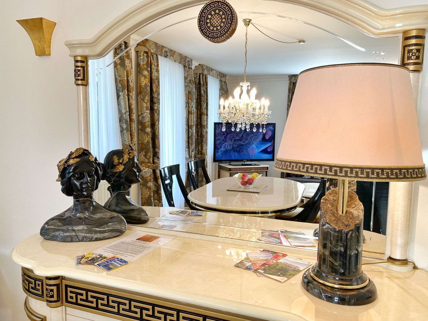 Ein stilvoller Essbereich mit Marmortisch, dekorativen Büsten, einer Chandelierleuchtre und einem Fernseher im Hintergrund.