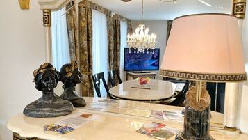 Ein stilvoller Essbereich mit Marmortisch, dekorativen Büsten, einer Chandelierleuchtre und einem Fernseher im Hintergrund.