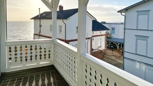 Un balcon avec vue sur la mer, des bâtiments blancs et une voiture garée à l’extérieur.