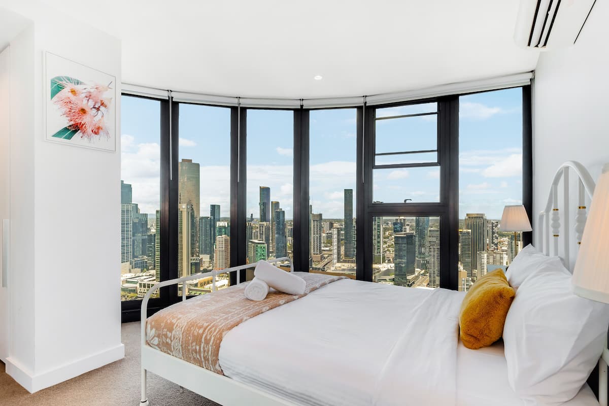 Quarto com vista para a cidade, uma cama, uma mesa de cabeceira e uma janela com persianas.