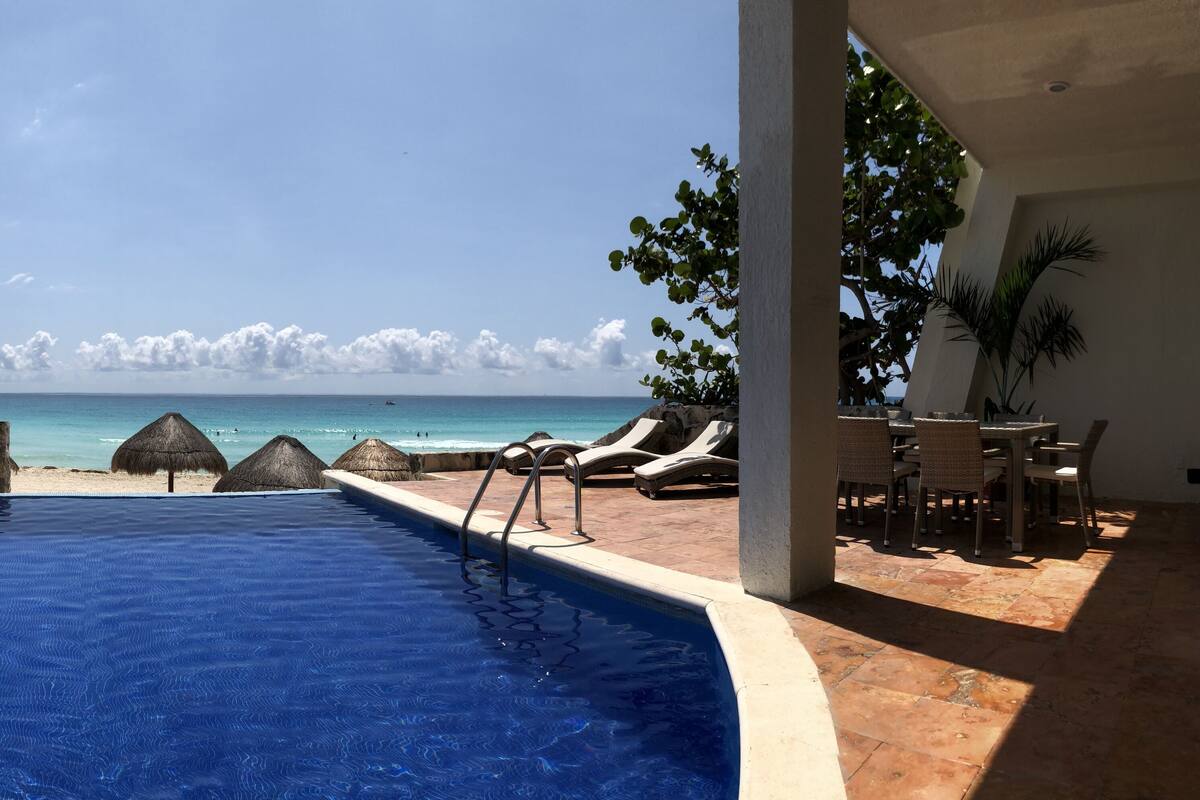 Una piscina con vista al océano, sillas de descanso y un área de comedor con mesas y sillas.