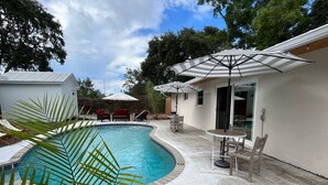 Ein Pool mit geschwungener Kante, umgeben von einer Terrasse mit Gartenmöbeln und Sonnenschirmen.