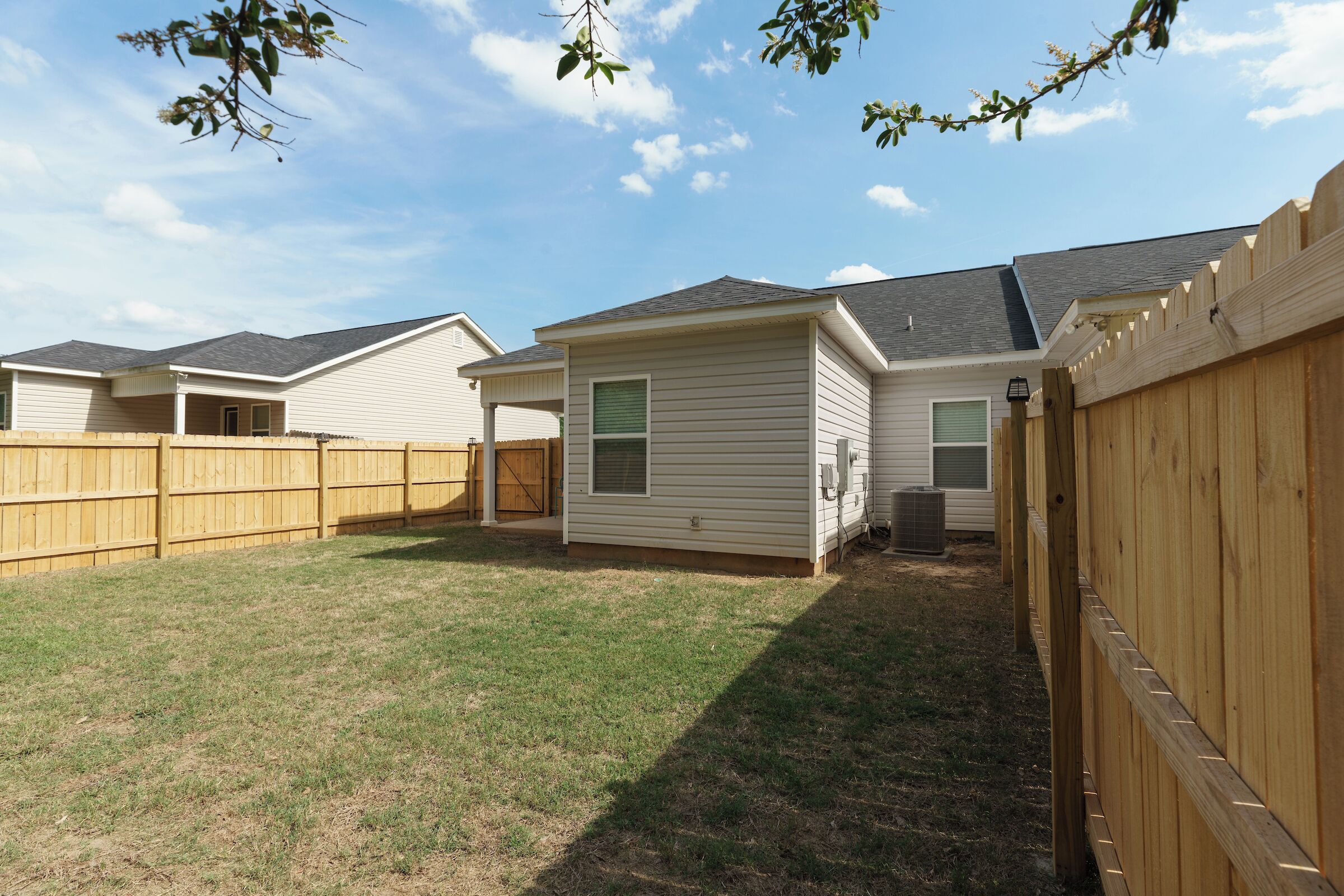 A residential backyard with a fenced area, a small shed, and a house with a sloped roof.