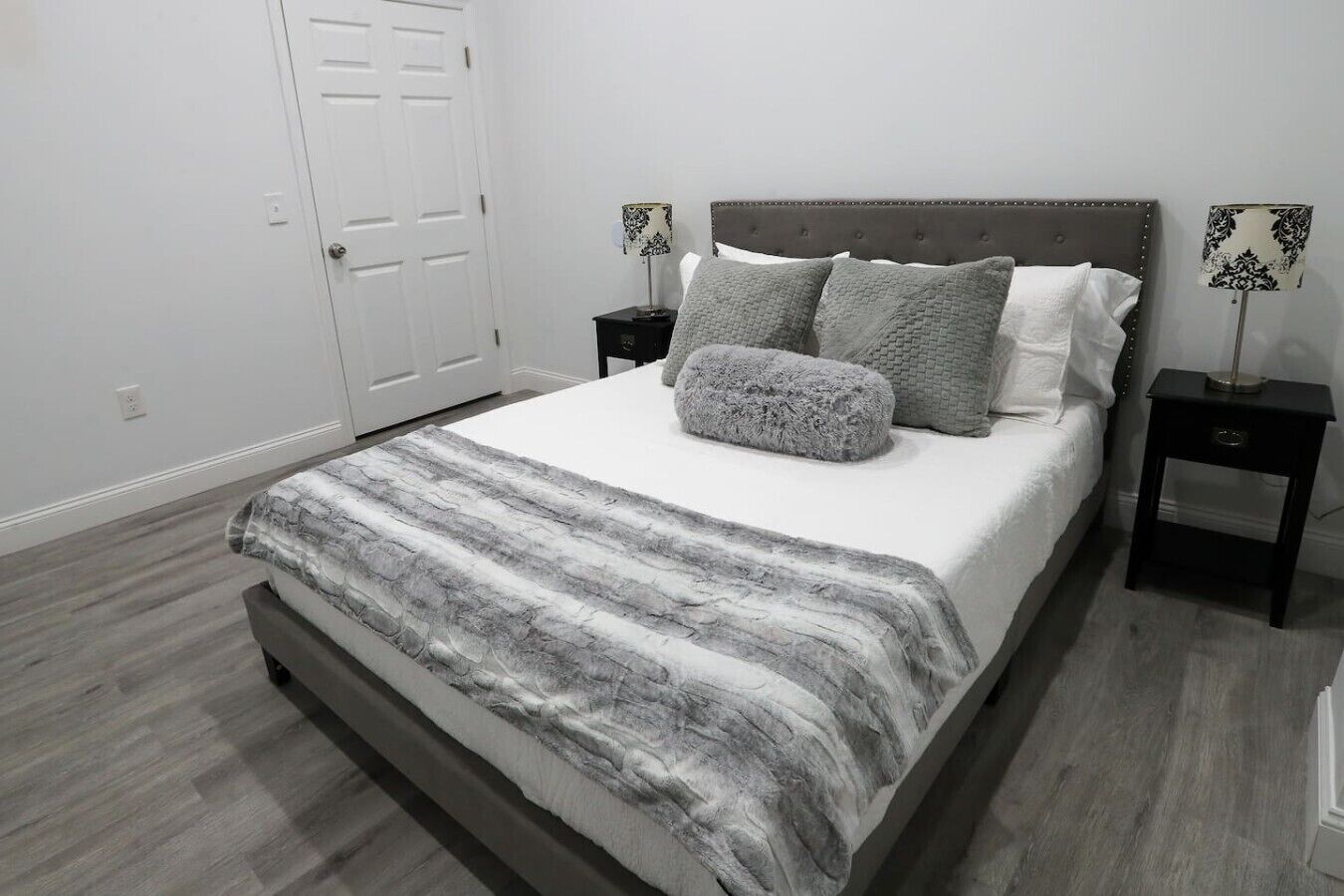 A bedroom with a bed, two nightstands, a door, and a lamp.