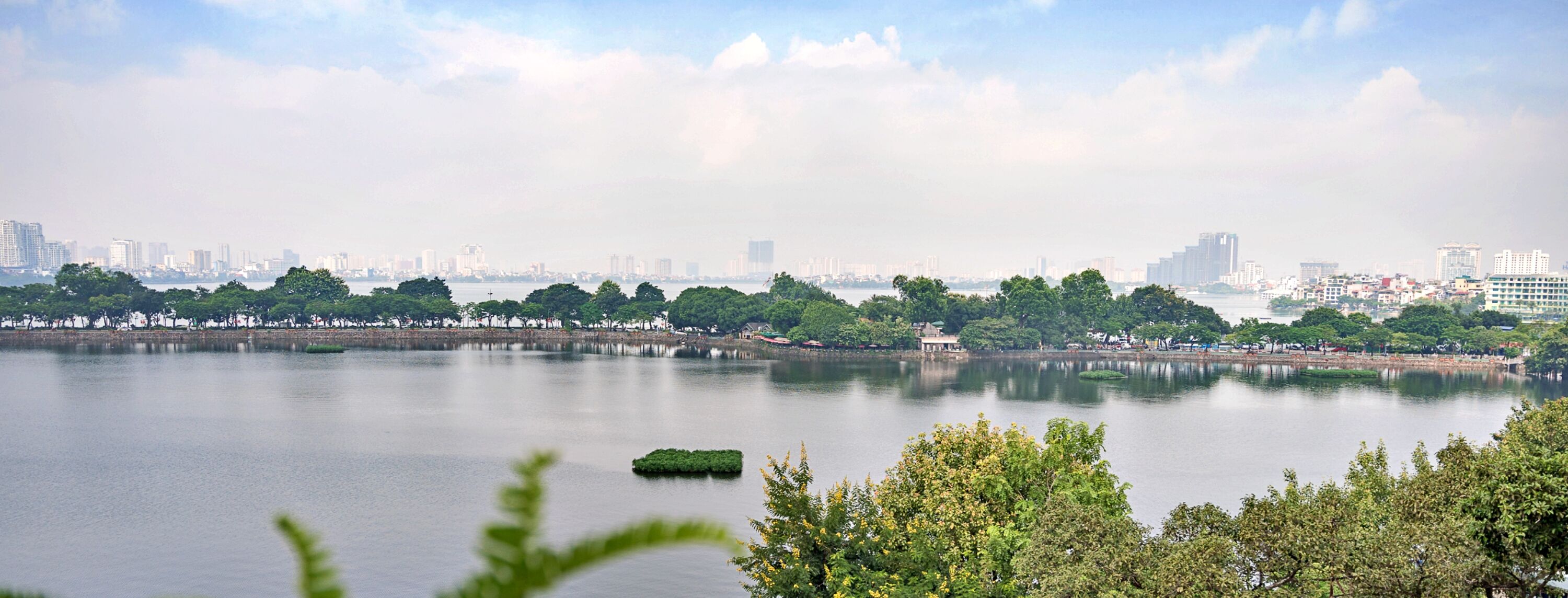 A calm lake with a city skyline in the background, surrounded by greenery.