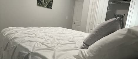 A bedroom with a large bed, a door to a walk-in closet, and a ceiling light.