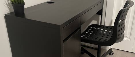 A black desk with a potted plant, a black office chair with wheels, and a white door in the background.