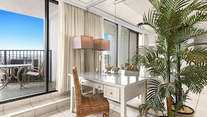 Un balcón con un comedor, una silla de mimbre, una mesa de vidrio, una lámpara y una planta grande en maceta.