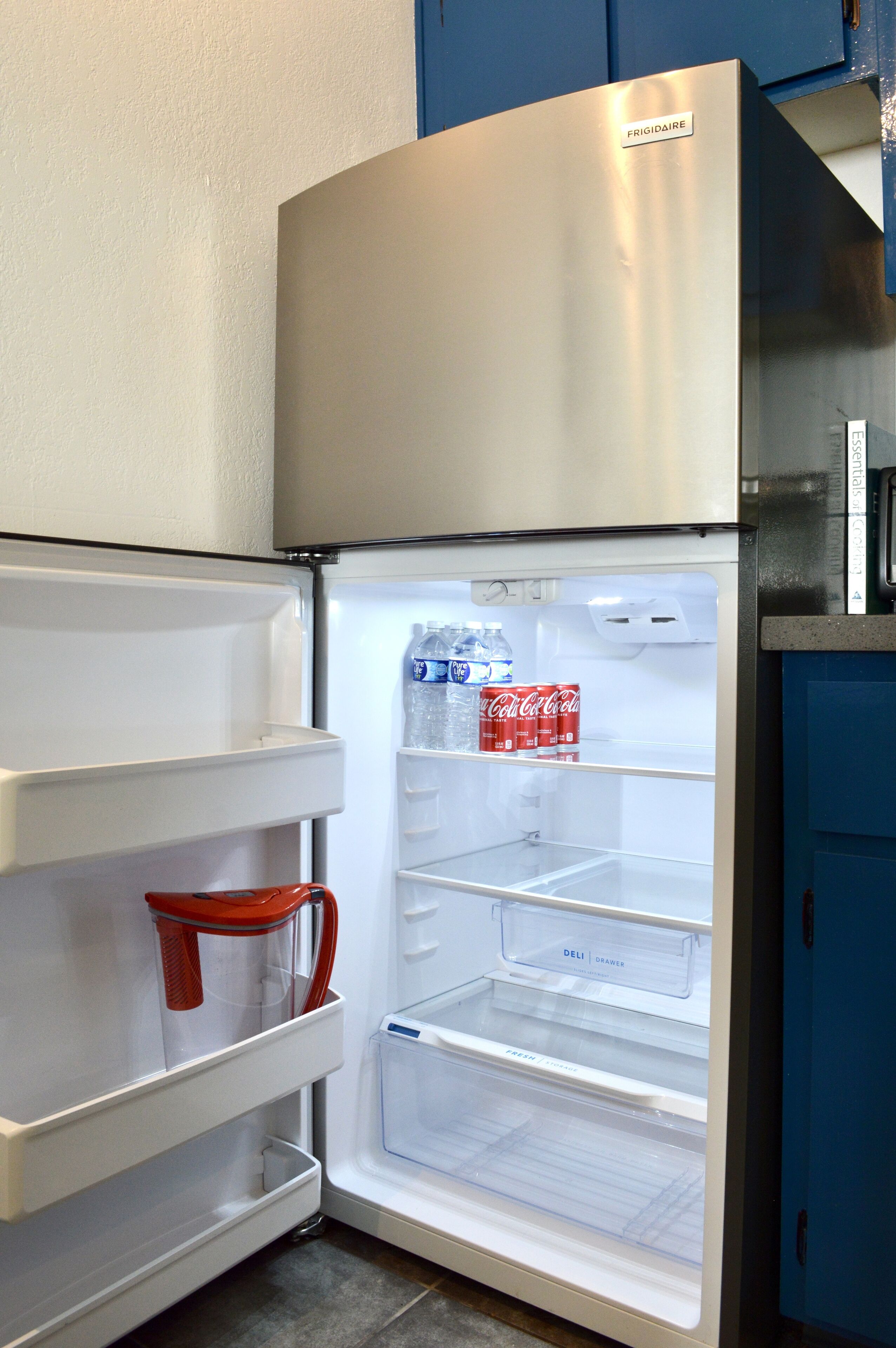 Un refrigerador de acero inoxidable con compartimento congelador a la izquierda, un cajón para alimentos frescos en la parte inferior y un cajón para embutidos en el centro.