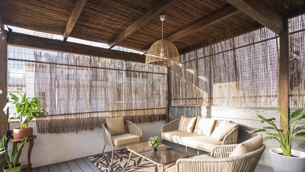 A covered outdoor seating area with wicker furniture, a woven ceiling, and a patterned floor rug.