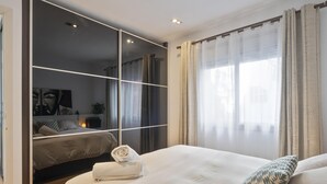 A modern bedroom with a large bed, a built-in wardrobe, and a large window with sheer curtains.