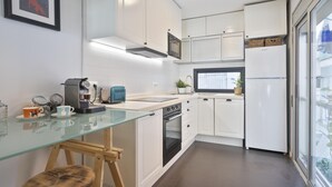 A modern kitchen with white cabinetry, a glass countertop, a built-in oven, and a window providing natural light.