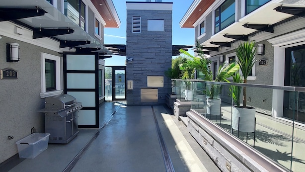 A modern building with a central tower, glass railings, and outdoor seating areas. - Beautiful Bright 3 Bedroom Townhouse  (Vancouver)