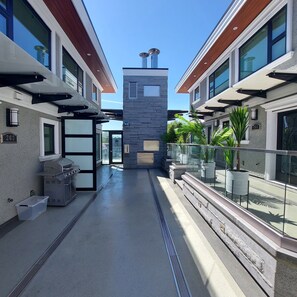 A modern outdoor corridor with a central stone structure, glass railings, and potted plants.