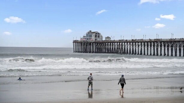 A beach with a pier extending into the ocean, a house on the pier, and people walking on the beach. - Cozy 1BR Bungalow by the beach, coffee, and dining (Oceanside)