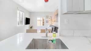 A modern kitchen with a white countertop, stainless steel sink, and a red pendant light. - Cozy 1BR Bungalow by the beach, coffee, and dining (Oceanside)