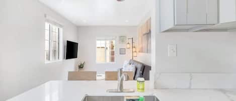 Cozinha moderna com bancada branca, pia de aço inoxidável e luminária pendente vermelha.