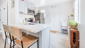 A modern kitchen with white cabinetry, a central island, and a built-in microwave. - Cozy 1BR Bungalow by the beach, coffee, and dining (Oceanside)