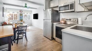 A modern kitchen with stainless steel appliances, a dining area with a wooden table and chairs, and a ceiling fan. - Cozy 2BR Bungalow by the beach, coffee, and dining. Walking Score 10/10 (Oceanside)