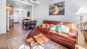 A living room with a red leather sofa, a wooden coffee table, and a dining area with a table and chairs. - Cozy 2BR Bungalow by the beach, coffee, and dining. Walking Score 10/10 (Oceanside)