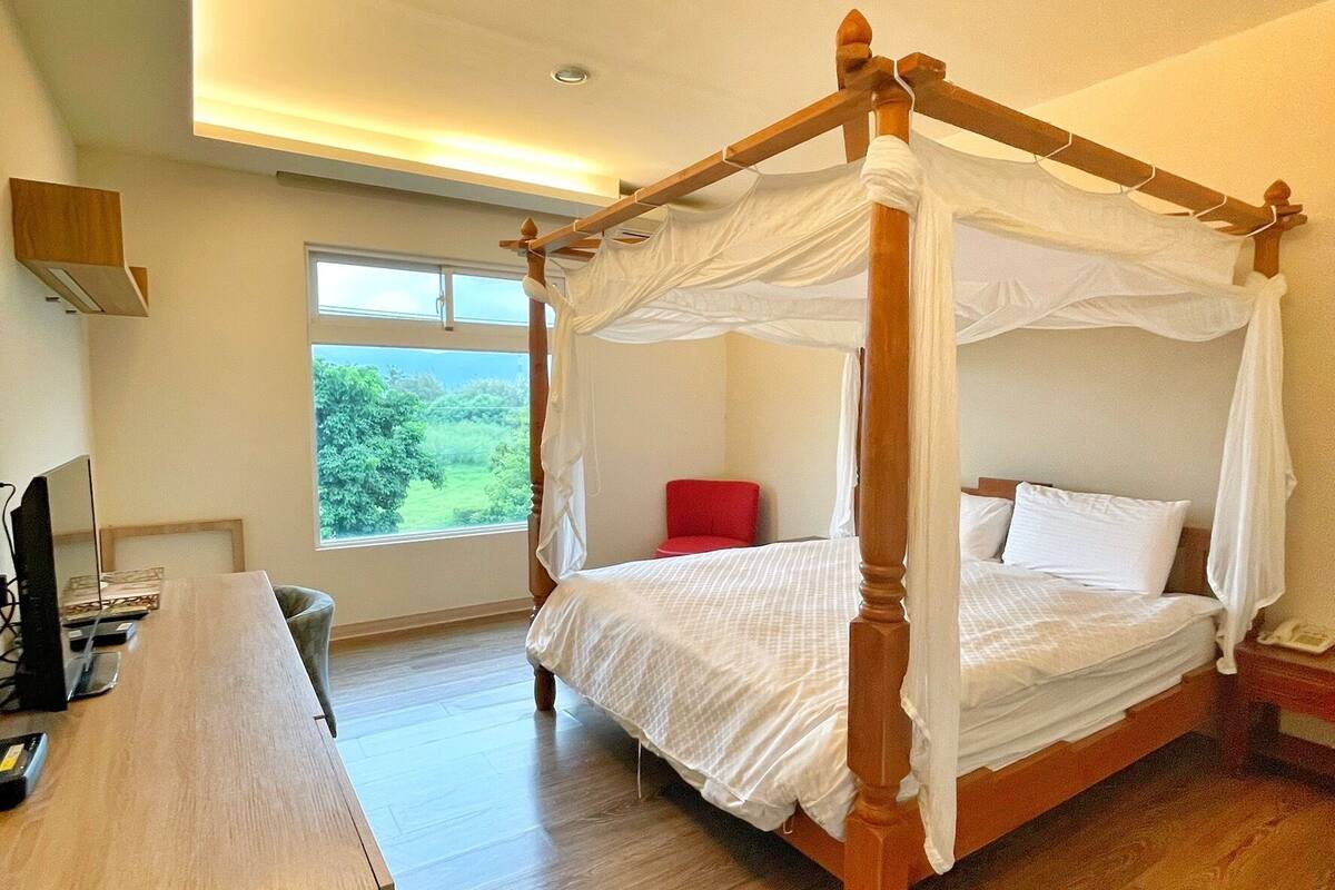 Un'ampia camera da letto con un letto a baldacchino, una scrivania in legno e una grande finestra con vista sul verde.