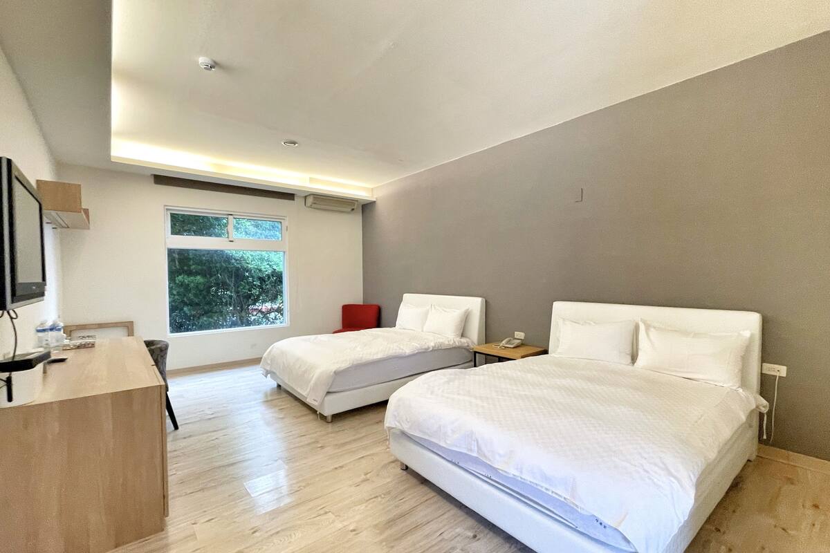 Una camera d'albergo moderna con due letti, una scrivania, una sedia e una finestra vista alberi.