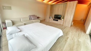 A modern bedroom with a large bed, a sofa, a TV, and wooden flooring. - Kenting Grandmas (Hengchun)