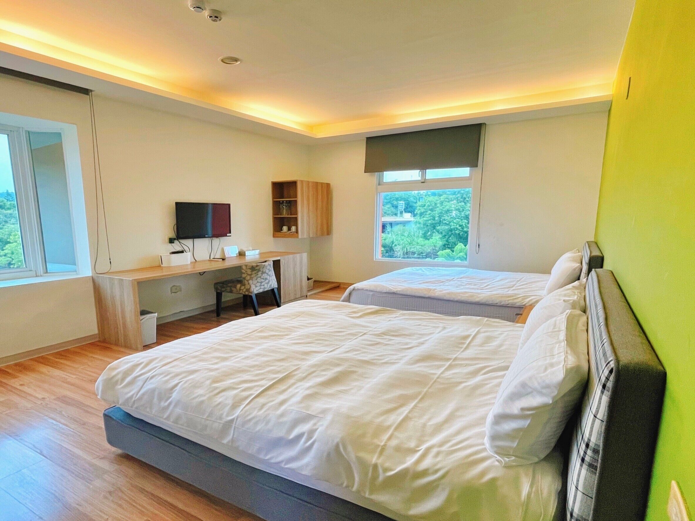Une chambre moderne avec deux lits, un bureau, une télévision et une fenêtre donnant sur un paysage verdoyant.