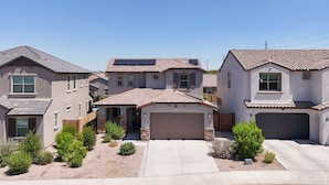 A residential area with houses featuring a mix of architectural styles, including a central house with a garage and solar panels, surrounded by smaller homes with similar roofing and landscaping.
