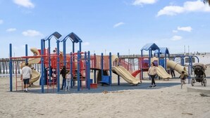 Een speeltuin met glijbanen en klimconstructies op een zandstrand.