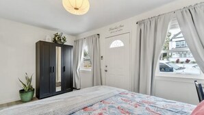 Een slaapkamer met een bed, een garderobe, een raam met gordijnen, een kamerplant en een muur met een bord.