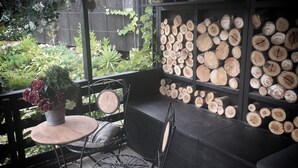 Un balcone con un tavolo rotondo e sedie, una pianta in vaso e mensole con legna ordinatamente impilata.