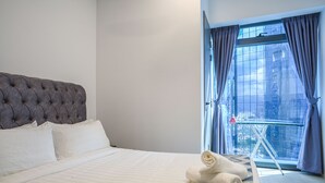 Habitación de hotel con una cama grande, vista a la ciudad a través de una ventana y una mesita con una toalla.