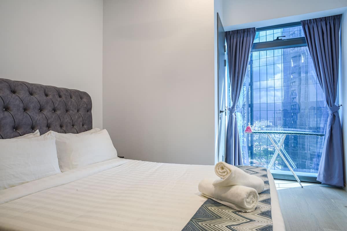 Ein Hotelzimmer mit einem großen Bett, Blick auf die Stadt durch ein Fenster und einem kleinen Tisch mit einem Handtuch.